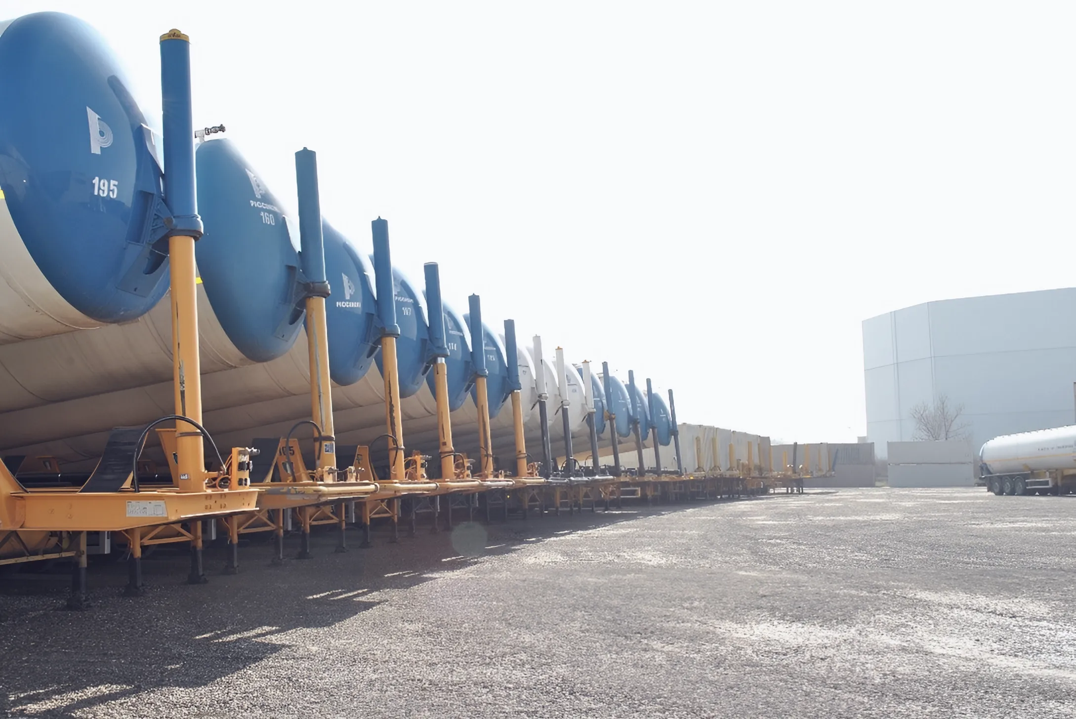 Long row of silo trailers with blue ends and yellow chassis parked in the yard