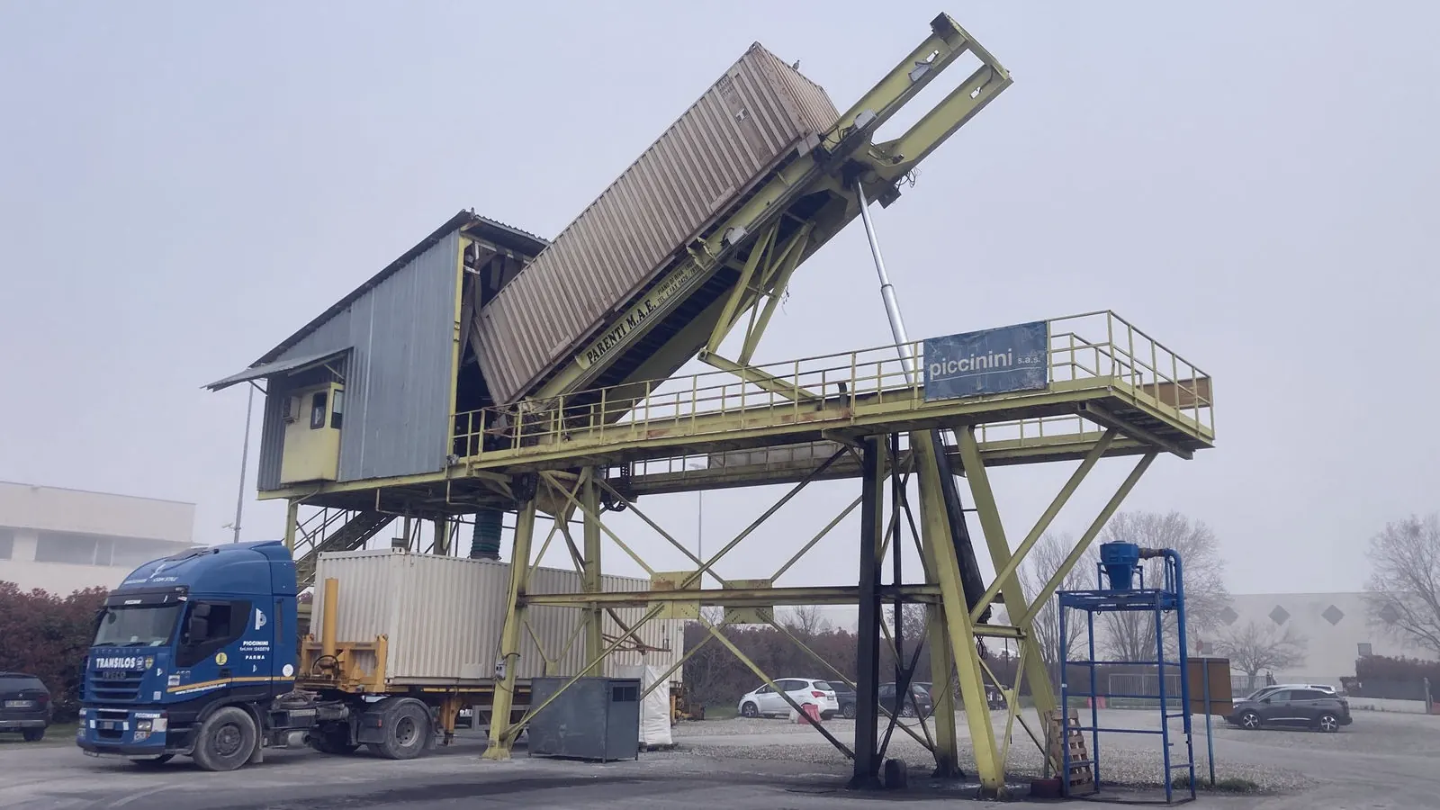 Container tilted on the depot’s yellow tipper, with a Transilos truck beneath
