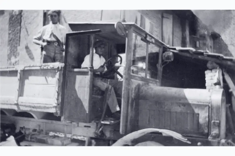 Black-and-white vintage photo: lorry with wooden body, driver at the wheel and a man on the back