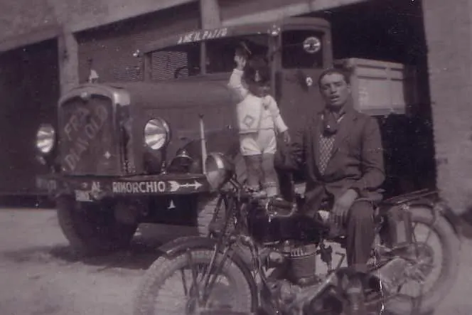 Vintage photo: man and child on a motorcycle in front of a lorry marked Al rimorchio