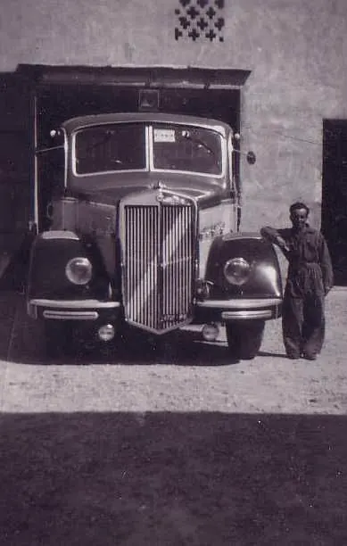 Driver in overalls leaning on a vintage lorry in front of the garage door