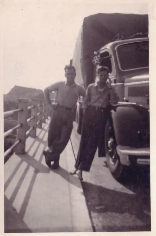 Two drivers posing on a bridge next to a tarpaulin lorry